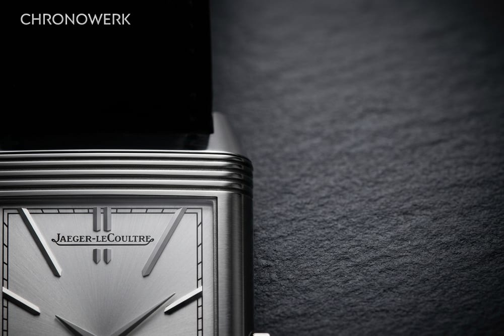 Ausschnitt eines rechteckigen Stahlgehäuses mit Godrons und silbernem Zifferblatt mit Signatur Jaeger-LeCoultre auf dunklem Schiefer
