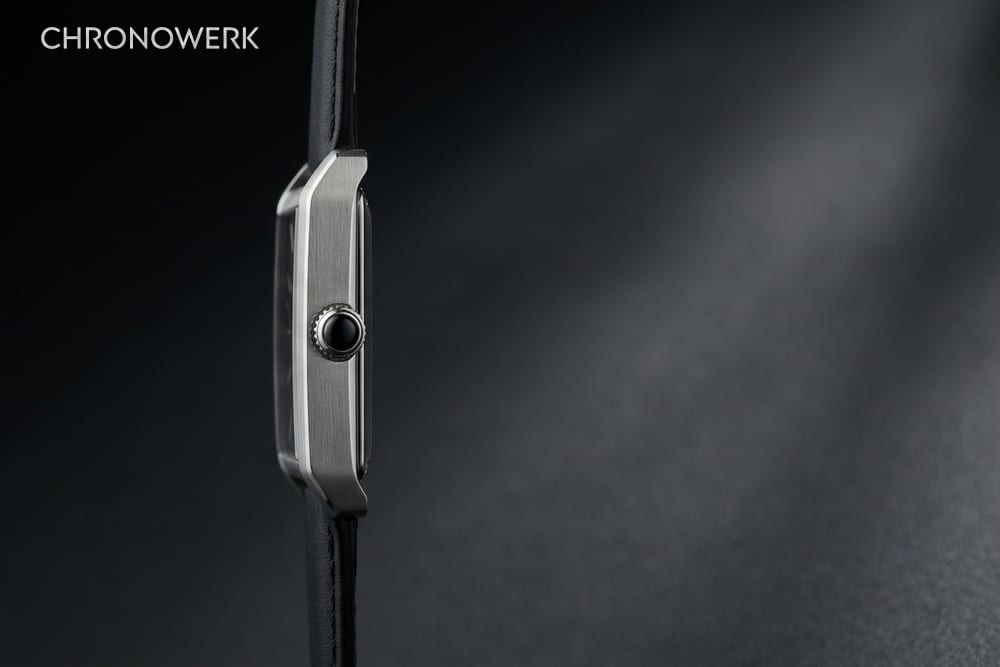 Rechteckige Edelstahluhr in Seitenansicht mit Cabochon-Krone links im Bild auf anthrazitfarbener Fläche – Header zum Cartier-Markenporträt